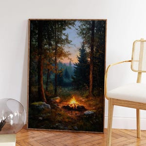 May include: A framed landscape painting depicts a campfire in a forest at dusk. The artwork features tall trees, a glowing fire, and a colorful sky. The painting is displayed on a wooden floor, with a modern chair in the background.