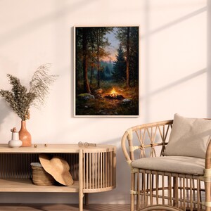 May include: A framed art print depicts a campfire scene in a forest. The artwork features a warm, inviting campfire with flames, surrounded by trees and rocks. The color palette includes greens, browns, and oranges, creating a cozy, natural ambiance.