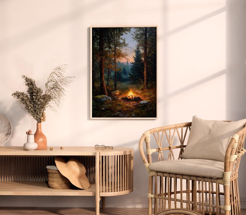 May include: A framed art print depicts a campfire scene in a forest. The artwork features a warm, inviting campfire with flames, surrounded by trees and rocks. The color palette includes greens, browns, and oranges, creating a cozy, natural ambiance.