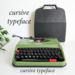 May include: A vintage green typewriter with black keys and red accents, alongside a black carrying case. The words "cursive typeface" are displayed above and below the typewriter.
