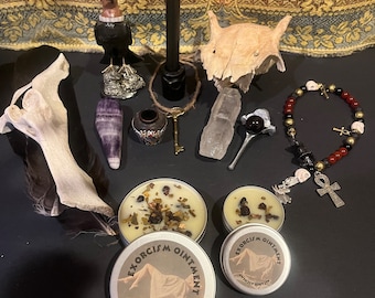 May include: A collection of occult and witchcraft items including two small jars of Exorcism Ointment, a black candle, a skull, a crystal, a feather, a bone, a key, a small jar, a bracelet, and an ankh.
