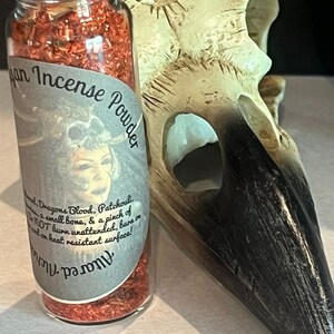 May include: A glass jar filled with red incense powder. The label reads "Pagan Incense Powder" and lists the ingredients: Dragons Blood, Patchouli, a small bone, and a pinch of something else. The label also states "Do NOT burn unattended, burn on heat resistant surface!"