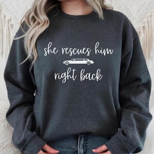 Op de afbeelding: Donkergrijze trui met witte tekst die "she rescues him right back" luidt en een wit silhouet van een limousine.