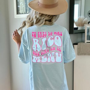 May include: A light blue t-shirt with a pink graphic that says "Tu eres lo mas rico que hay en el menu" in a retro font.