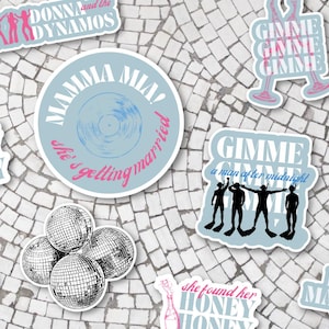 May include: A collection of colorful stickers featuring various song titles and lyrics from the musical Mamma Mia! The stickers are printed on white paper with a blue and pink color scheme. The stickers feature text such as "Dancing Queen", "Mamma Mia!", "Gimme! Gimme! Gimme!" and "Honey Honey".