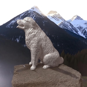 May include: A white ceramic sculpture of a dog sitting on a rock with a mountain range in the background.