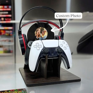 Könnte beinhalten: Ein schwarz-weißer Videospiel-Controller-Ständer mit einem schwarzen Headset und einem runden Fotorahmen mit einem Familienfoto. Der Ständer ist aus Holz und hat eine schwarze Oberfläche. "Custom Photo" steht auf dem Bild.