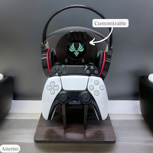 Puede incluir: Un soporte de madera negro con un diseño personalizable que presenta un logotipo verde y rojo. El soporte sostiene un mando de PlayStation 5 blanco y unos auriculares negros con detalles rojos. El texto "Customizable" está escrito en la imagen.