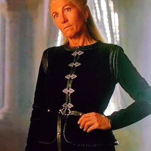 May include: A black velvet jacket with silver-colored embellishments and a matching belt. The jacket has long sleeves and a high neckline. The silver embellishments are ornate and detailed. The jacket is worn by a person with blonde hair.