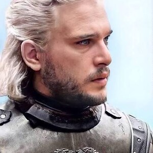 May include: A man with long, light blonde hair and a short beard, wearing a silver and black chest plate with two wolf emblems. The man has blue eyes and is looking off to the side.