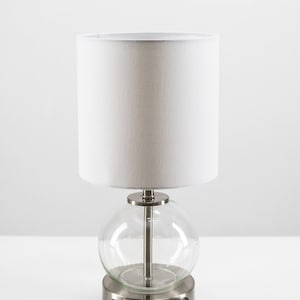 May include: A silver table lamp with a white fabric shade and a clear glass globe base. The base has a built-in power outlet with two USB ports and a standard outlet.