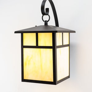 May include: A black metal outdoor wall sconce with a square, frosted glass shade. The sconce has a decorative scroll design on the top.