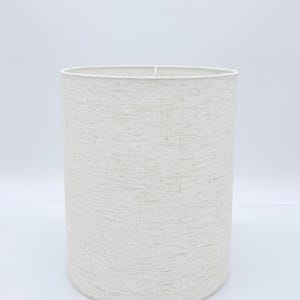 May include: A cylindrical lampshade with a textured, off-white fabric. The lampshade has a simple, clean design and is suitable for various lamp bases. The neutral color and minimalist style make it versatile for different interior decor styles.