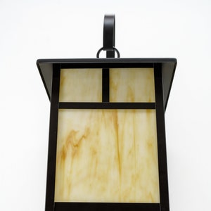 May include: A black metal outdoor wall light fixture with a frosted glass shade. The glass has a marbled pattern in shades of yellow and white.