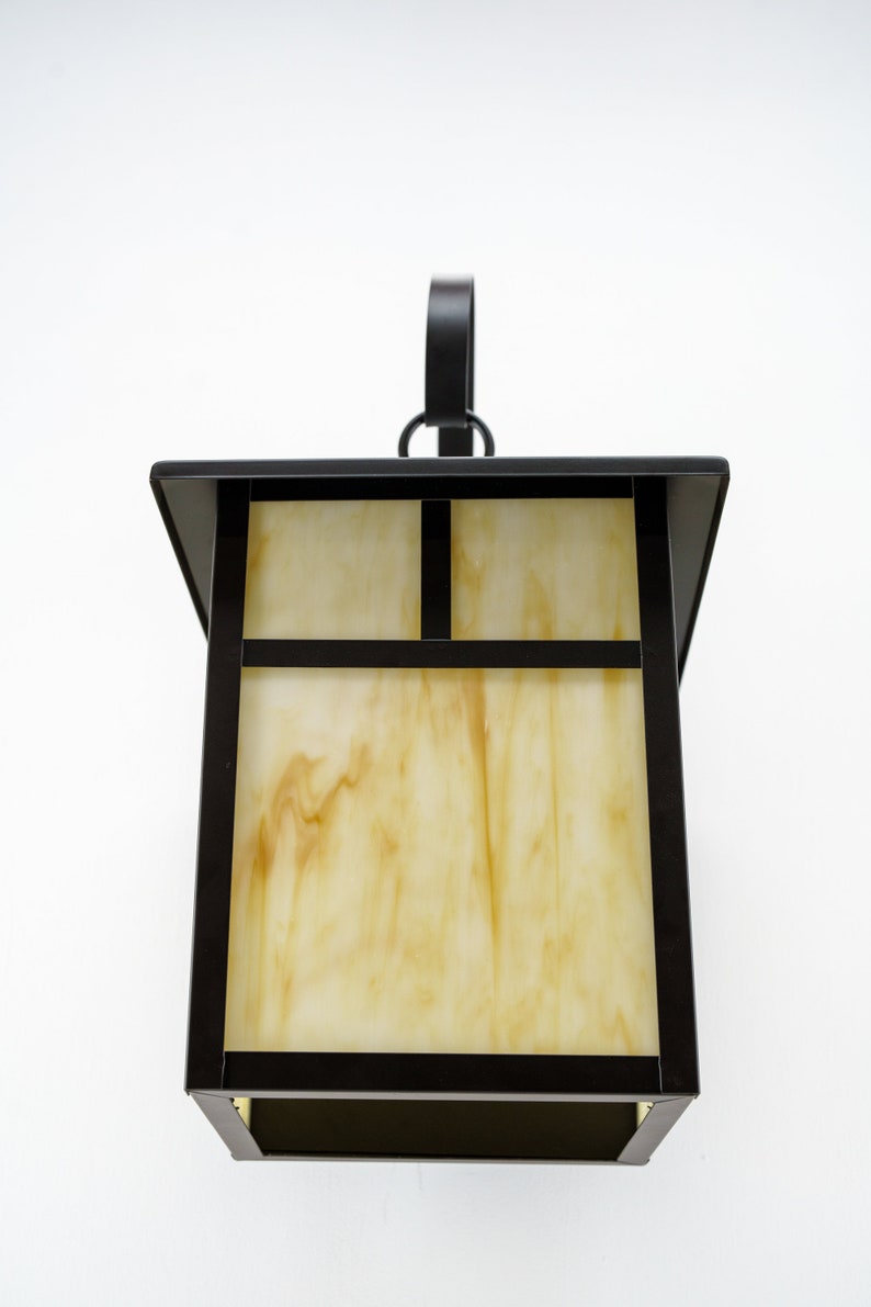 May include: A black metal outdoor wall light fixture with a frosted glass shade. The glass has a marbled pattern in shades of yellow and white.