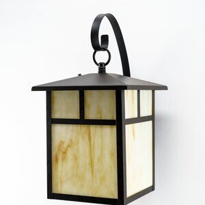 May include: A black metal outdoor wall light fixture with a frosted glass shade. The light has a decorative scroll design on the top.