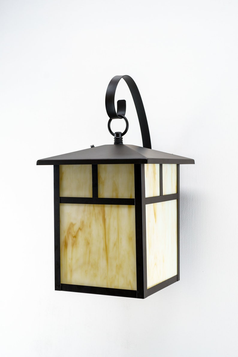 May include: A black metal outdoor wall light fixture with a frosted glass shade. The light has a decorative scroll design on the top.