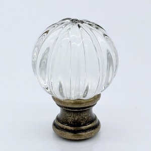 May include: Clear glass cabinet knob with a ribbed, pumpkin-shaped design. The knob sits on a bronze-colored base. This decorative hardware is suitable for drawers, cabinets, or furniture.