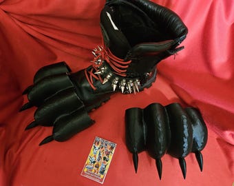 May include: Black leather boots with red laces and silver studs. The boots have a claw-like design on the front and back. The boots are on a red surface.