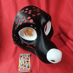 May include: Black and white furry mask with a white nose and eyes. The mask is made of a lightweight material and has a mesh design. The mask is for sale by Metalhound Studios, a fursuit maker.