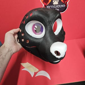 May include: A black 3D-printed animal mask featuring a white nose, large eye sockets with a purple and pink iris design, and a mesh screen. The mask has a textured surface with circular ventilation holes along the side and two separate white pieces.