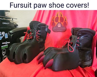 May include: Black faux fur paw shoe covers with red laces and claws. The covers are designed to fit over boots, creating a unique furry look. The image includes the text "Fursuit paw shoe covers!"