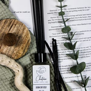 Może przedstawiać: Dyfuzor zapachowy z czarnymi patyczkami, butelką z napisem "Chateau" i laską wanilii. Butelka ma 150 ml / 7 oz. Dyfuzor otoczony jest książką, drewnianym plastrem i zielenią.