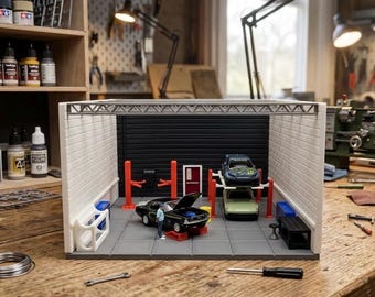 Può includere: Un diorama di garage in miniatura con un'auto sportiva nera dal cofano aperto, un'auto verde chiaro su un ponte sollevatore a due colonne e un'auto blu su un secondo ponte. La struttura presenta pareti in mattoni bianchi e colonne rosse.
