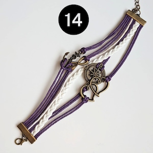 May include: Purple and white braided bracelet with an anchor, compass, and two hearts charms. The bracelet has a clasp closure.