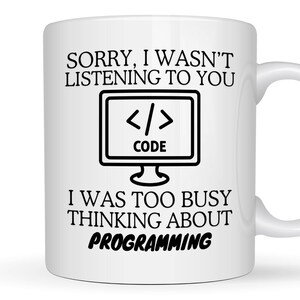 May include: White ceramic mug with black text. The mug features the words "SORRY, I WASN'T LISTENING TO YOU" above a computer monitor graphic with the word "CODE" and code symbols. Below the graphic, the text continues, "I WAS TOO BUSY THINKING ABOUT PROGRAMMING."