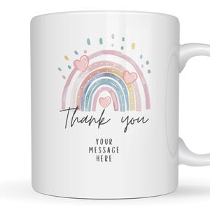 May include: A white ceramic mug featuring a pastel-coloured rainbow illustration with three small pink hearts and colourful dots above it. Below the rainbow, the text reads Thank you and YOUR MESSAGE HERE in a simple black sans-serif font.