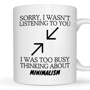 May include: White ceramic mug with a curved handle. The mug features black text that reads "SORRY, I WASN'T LISTENING TO YOU" above two black arrows and the text "I WAS TOO BUSY THINKING ABOUT MINIMALISM."