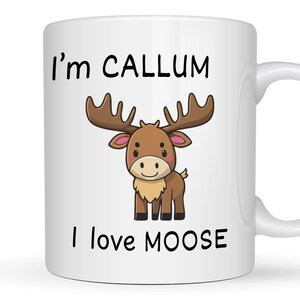 May include: A white ceramic mug featuring a cartoon illustration of a brown moose with large antlers. The text "I'm CALLUM" is printed in black above the moose, and the text "I love MOOSE" is printed in black below the moose illustration.