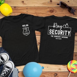 May include: Two black t-shirts with white text. The front shirt says "Nolan Ring Security" with a badge graphic. The back shirt says "Ring Security The Johnson's Wedding 06.24.2024".