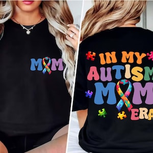 May include: Black t-shirt with a rainbow puzzle piece ribbon and the text "MOM" on the front. The back of the shirt has the text "IN MY AUTISM MOM ERA" with rainbow puzzle pieces.