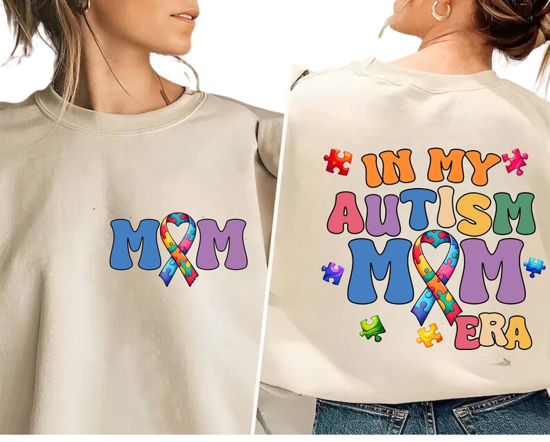 May include: A beige sweatshirt with a colorful puzzle piece ribbon and the text "MOM" on the front. The back of the sweatshirt has the text "IN MY AUTISM MOM ERA" with a colorful puzzle piece ribbon.
