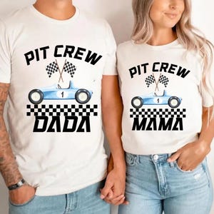Peut inclure: T-shirts blancs sur le thème de la course automobile. Chaque t-shirt présente un dessin de voiture de course bleu clair avec le numéro 1, des drapeaux à damiers et les mots "PIT CREW" au-dessus de la voiture. Un t-shirt dit "DADA" et l'autre "MAMA".