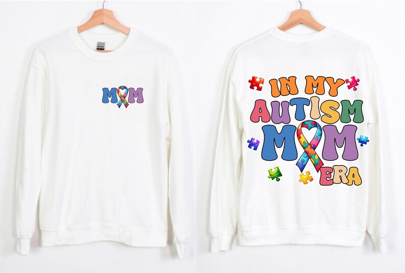 May include: White long-sleeved sweatshirt with a colorful puzzle piece ribbon and the text "MOM" on the front. The back of the sweatshirt has the text "IN MY AUTISM MOM ERA" with a colorful puzzle piece ribbon and puzzle pieces.