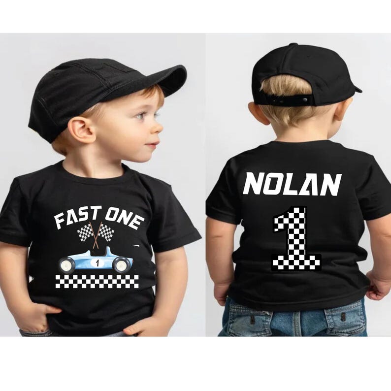 May include: Two black t-shirts with a racing car theme. One shirt says "Fast One" with a blue race car and checkered flags. The other shirt has the name "Nolan" and the number "1" with a checkered flag design.