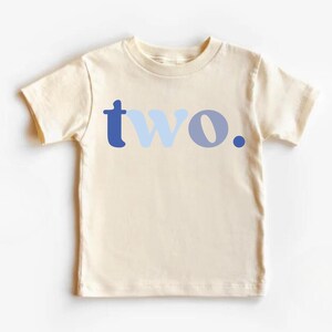 May include: Cream-colored toddler t-shirt with the word "two" in blue hues. The word is stylized with a dark blue "t", light blue "w", and a medium blue "o" with a dark blue period. A simple, yet stylish design.