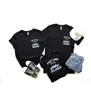 May include: Three black t-shirts with a racing car design. The shirts say "Pit Crew Mama", "Pit Crew Dada", and "Fast One Elijah".