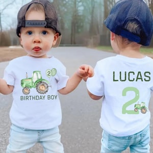 May include: Two white t-shirts with a green tractor design. One shirt says "Birthday Boy" and the other says "Lucas 2".