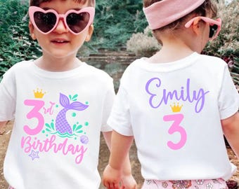 May include: White t-shirts with a mermaid design for a 3rd birthday celebration. The front displays a pink "3rd Birthday" graphic with a mermaid tail. The back of the shirt has the name "Emily" and the number "3".