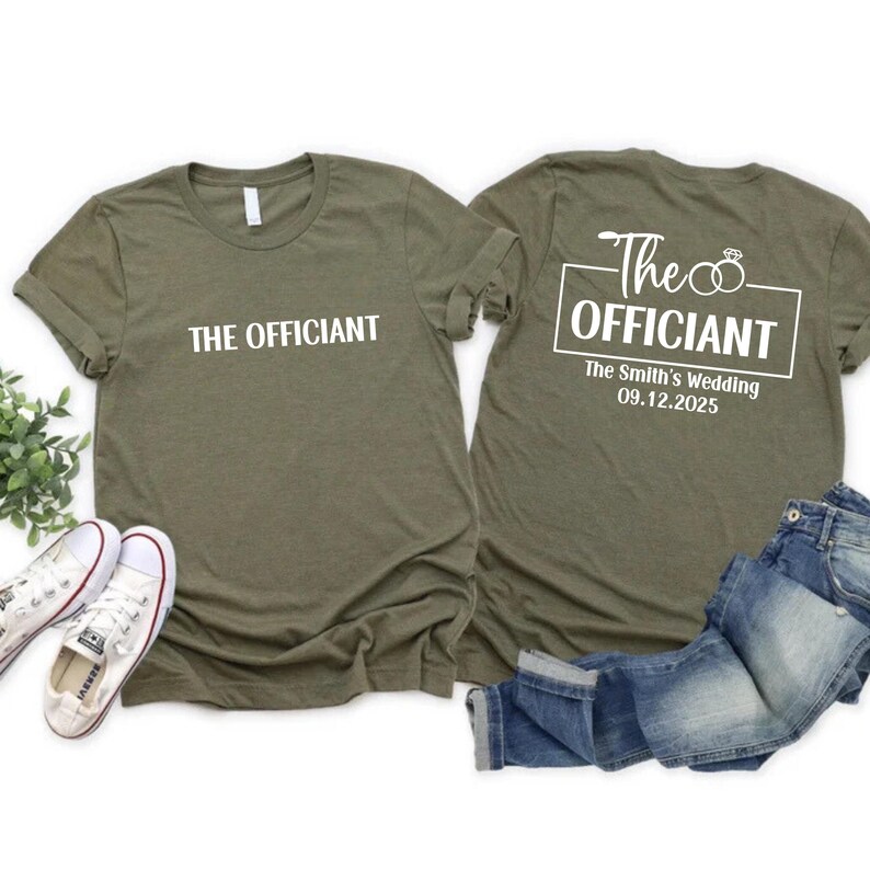 May include: Two olive green t-shirts with white text. The front of one shirt says "THE OFFICIANT". The back of the other shirt says "The OFFICIANT" with two rings and "The Smith's Wedding 09.12.2025" underneath.