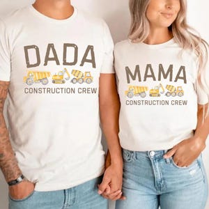 Peut inclure: Deux t-shirts blanc cassé avec des motifs assortis. L'un dit "DADA" et l'autre "MAMA" en lettres marron. En dessous, des illustrations de véhicules de chantier. Le texte "CONSTRUCTION CREW" est en dessous.