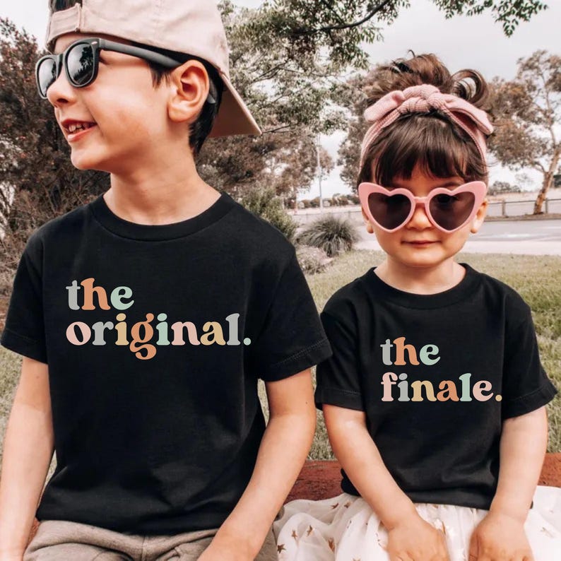 May include: Two children wearing black t-shirts with the phrases "the original" and "the finale" printed in pastel colors. The child on the left wears sunglasses and a cap, while the child on the right wears heart-shaped sunglasses and a headband.