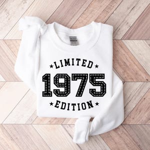 May include: White sweatshirt with black text that reads "*LIMITED* 1975 *EDITION*" with stars on either side of the text.
