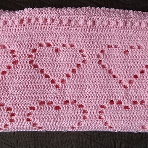 May include: A pink crocheted baby blanket with a heart pattern.