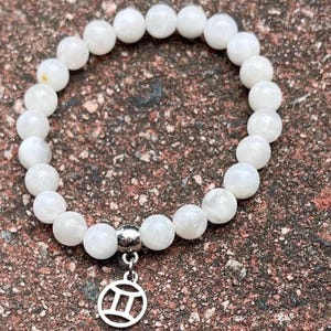 May include: White moonstone bead bracelet with a silver Gemini zodiac charm.