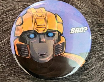 Puede incluir: Botón redondo con una ilustración de dibujos animados de la cara de un robot, con colores amarillo y gris con ojos azules. El botón tiene la palabra "BRO?" en texto blanco sobre un fondo azul.